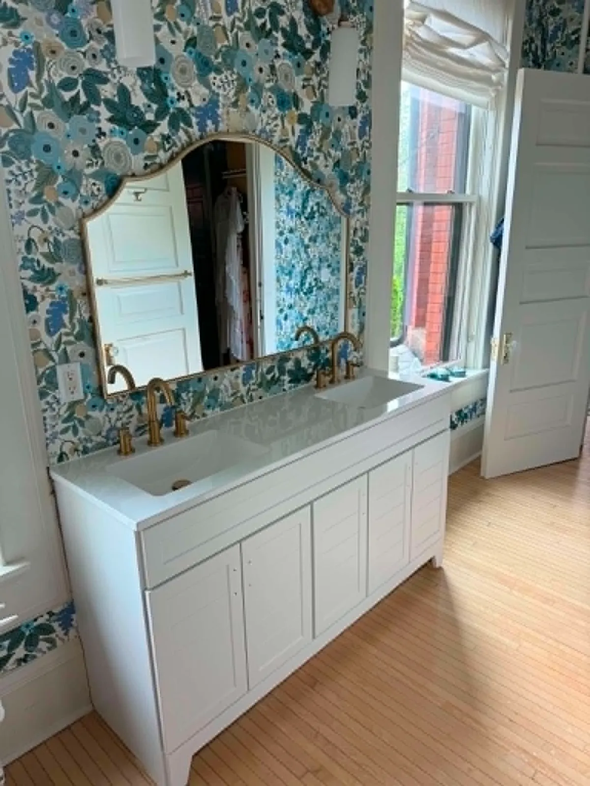 Remodeled bathroom vanity with double sinks, brass faucets, and an arched mirror